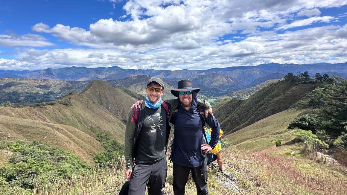 Will and Alex smiling in front of a layered landscape of lush jungle covered mountains in Ecuador