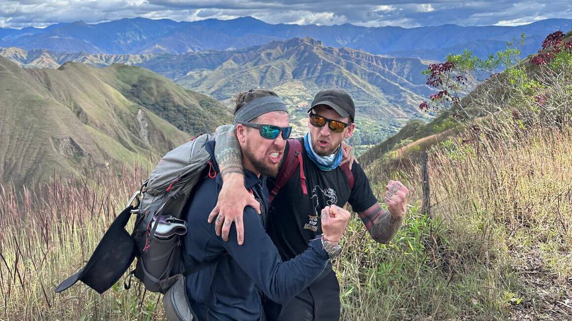 Will and Alex doing silly poses in front of a layered landscape of lush jungle covered mountains in Ecuador