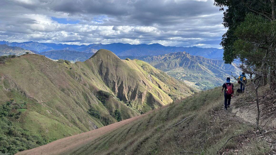 Two people hiking along a thin trail with lush jungle covered mountains in the distance in Ecuador