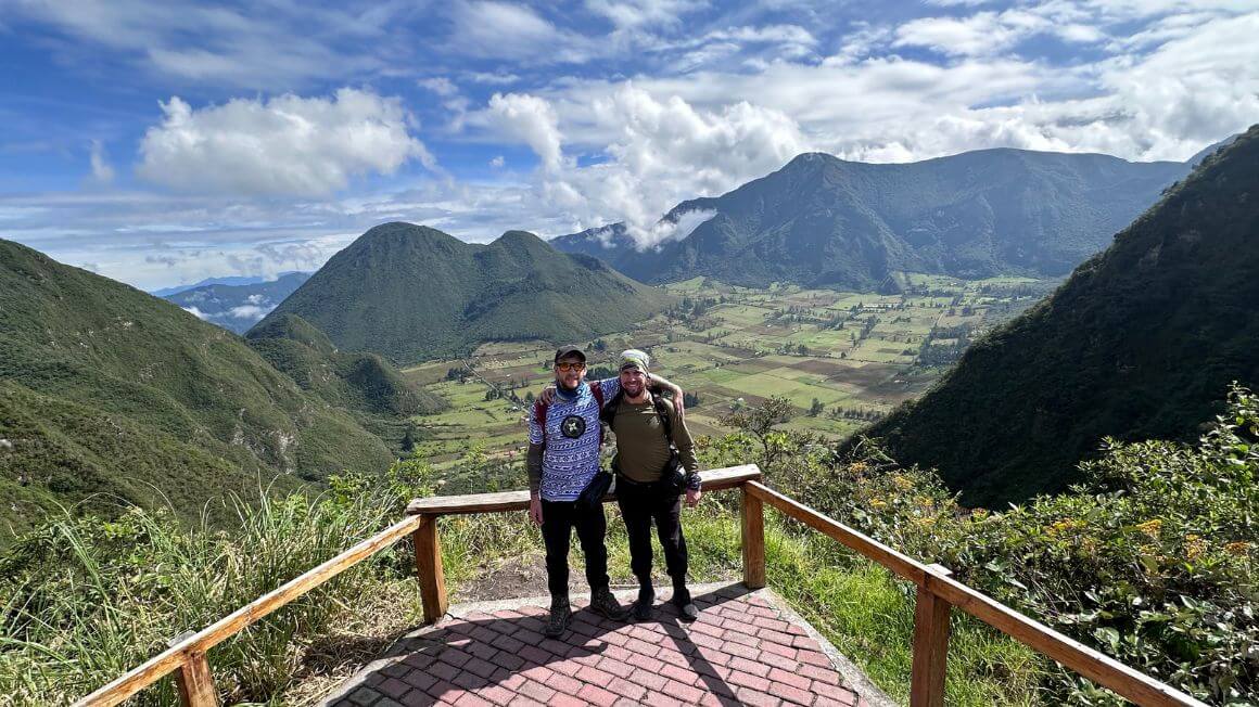 Will and Alex standing on a view point overlooking the lush mountains of Ecuador and farmed fields in the valleys below