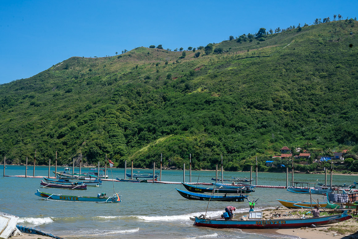 blue boats floating on almost clear turquoise water with a lush forested ridge towering behind it in kuta lombok