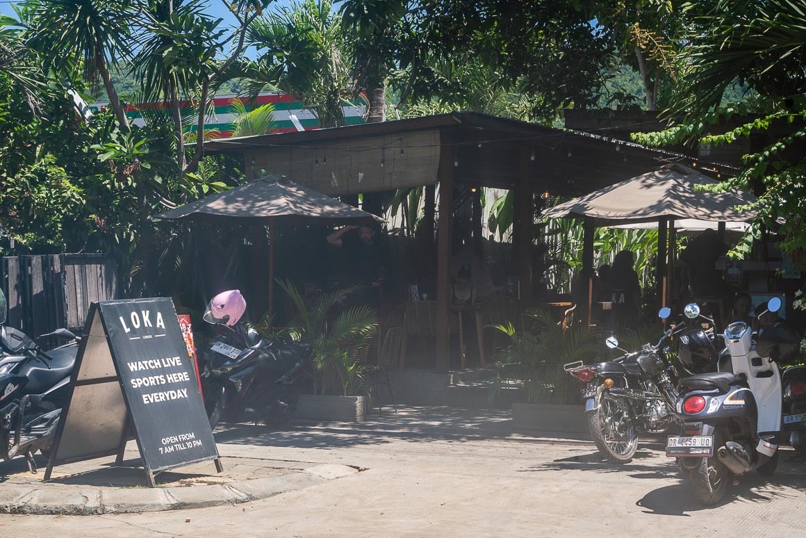 a hazy photo of the outside of a cafe with people and scooters working and eating in kuta lombok