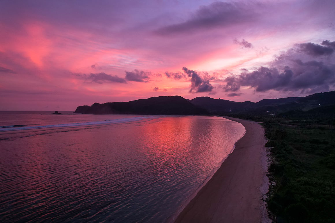 a bright pink and purple sunset over a beautiful beach in lombok as scene from a drone