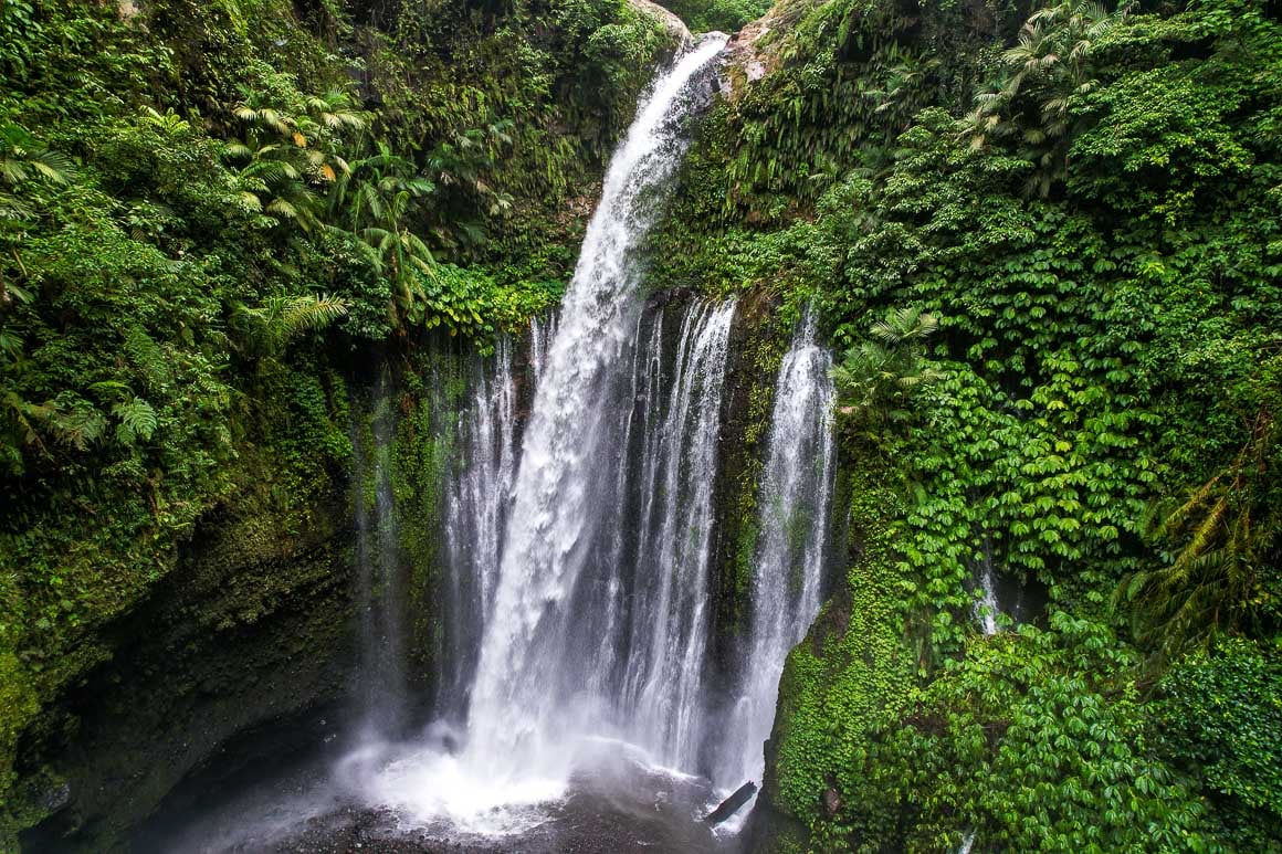 nearly half a dozen cascades of waterfalls pouring down a lush forested rock wall into a pool in north lombok indonesia