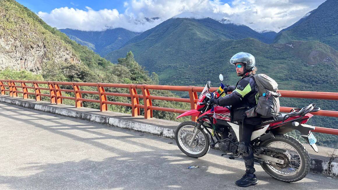 Will on a motorbike on a bridge crossing through the cloud enveloped jungle covered mountains of Peru