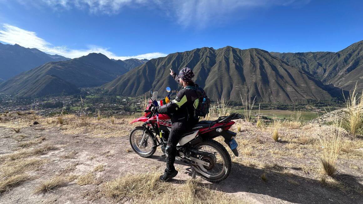 Will on a motorbike high above a town below with jungle covered mountains in the background