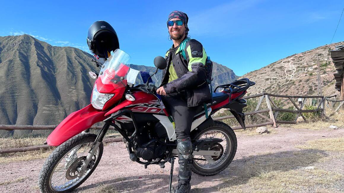 Will on a motorbike high above a town below with jungle covered mountains in the background