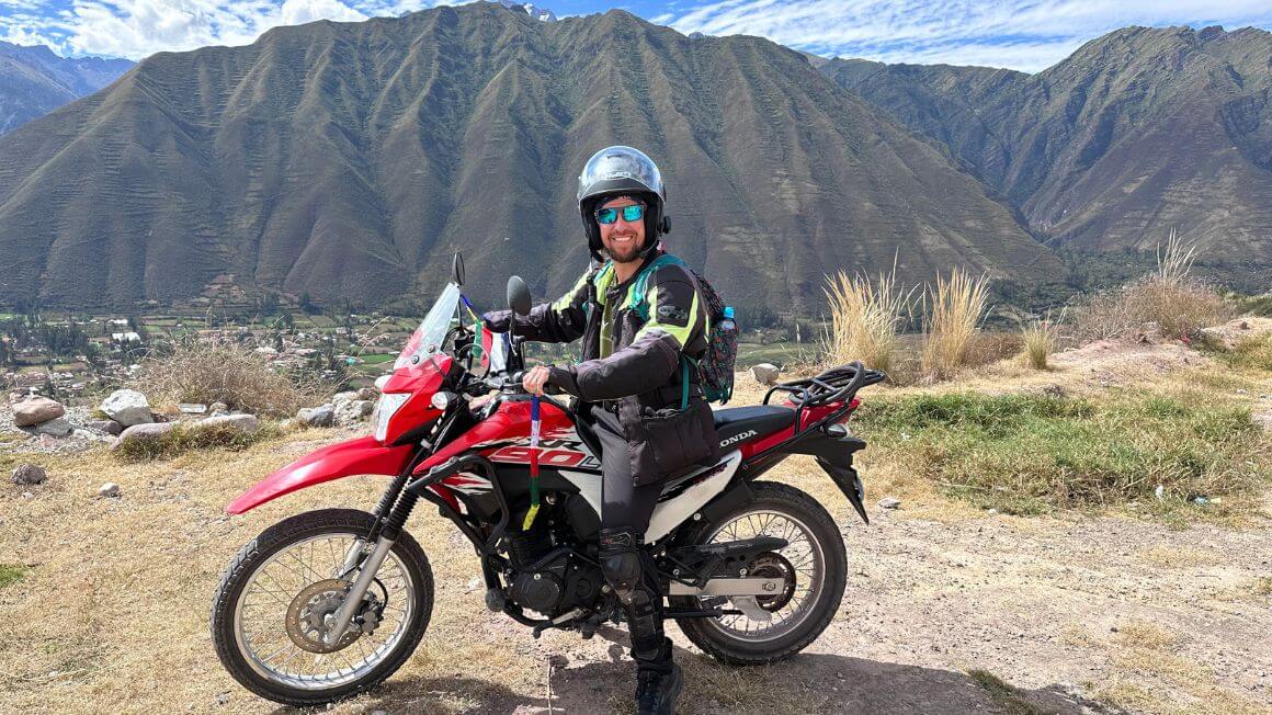 Will on a motorbike high above a town below with jungle covered mountains in the background