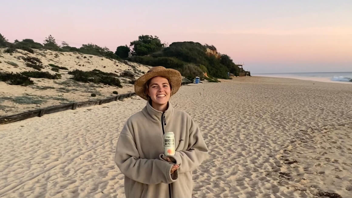 dani at the beach in faro portugal in november with jumper and a hat on at sunset