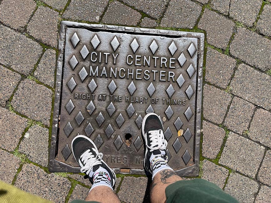 A person standing on a grid that reads "City Centre, Manchester. Right at the heart of things" in Manchester, England, United Kingdom.