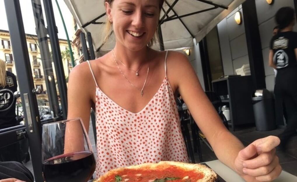 A woman smiling lovingly at a pizza in Italy with a glass of red wine