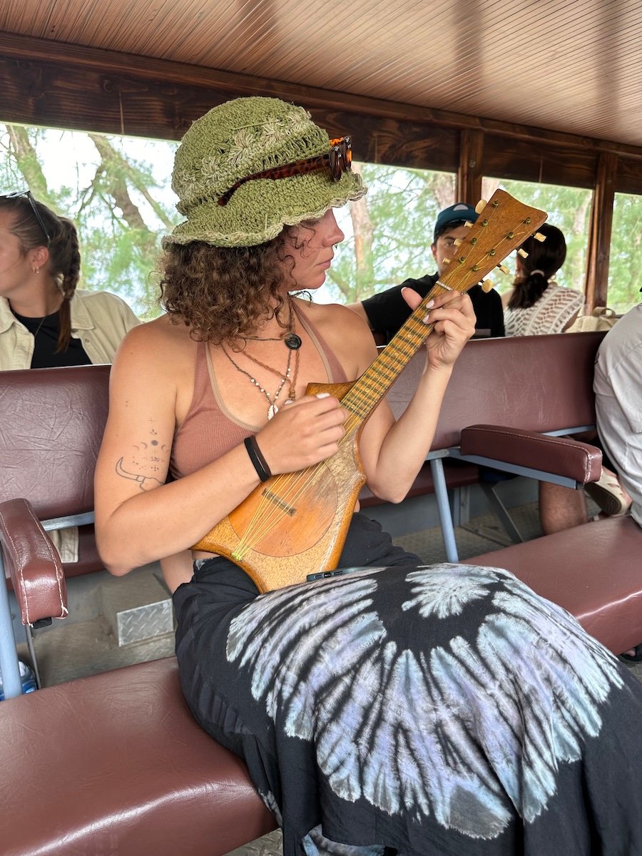 audy playing the ukelele while sitting on a leather bench on a boat in french polynesia