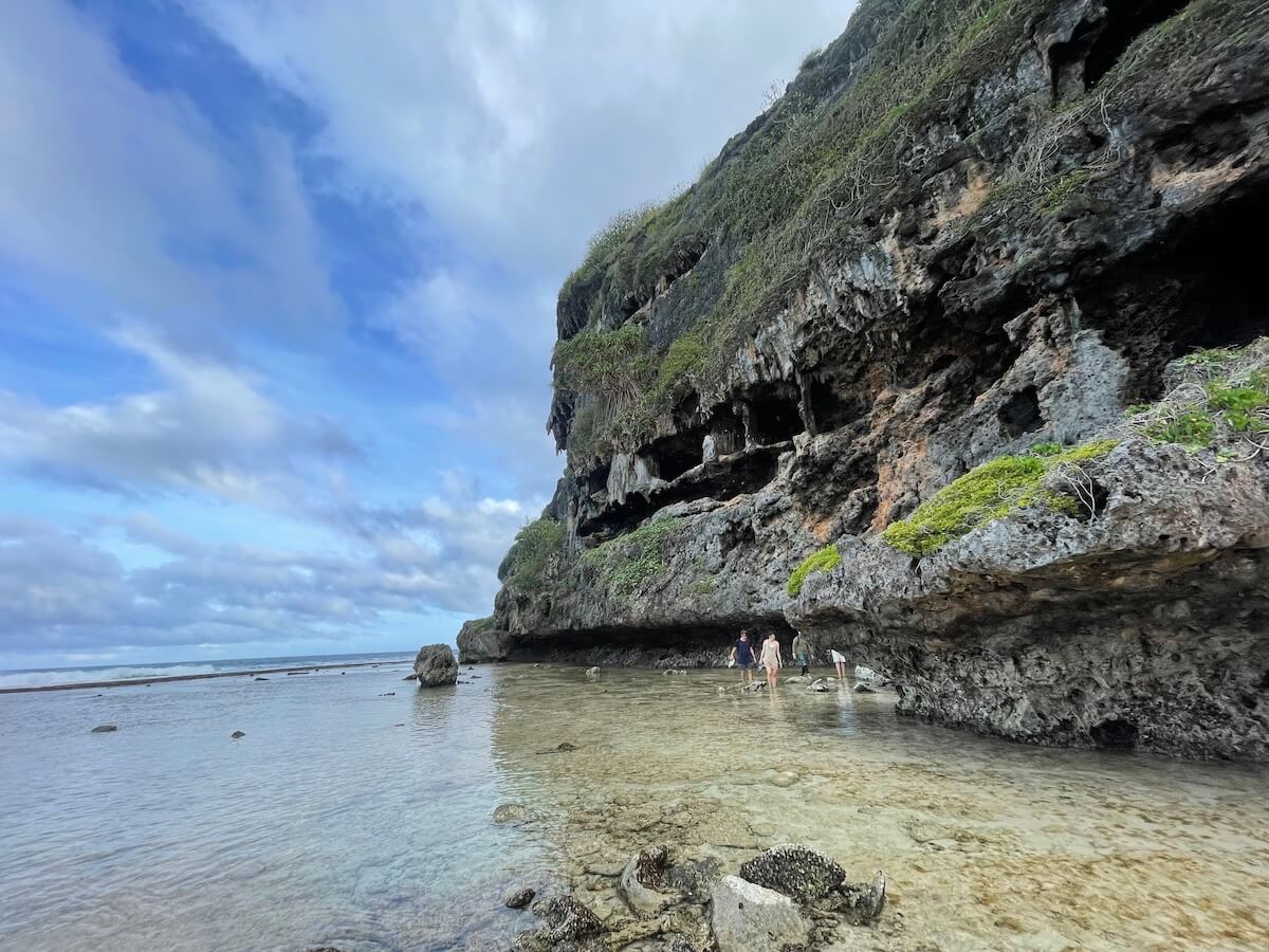 people walking in the shallow sea water beneath cliffs in rurutu french polynesia