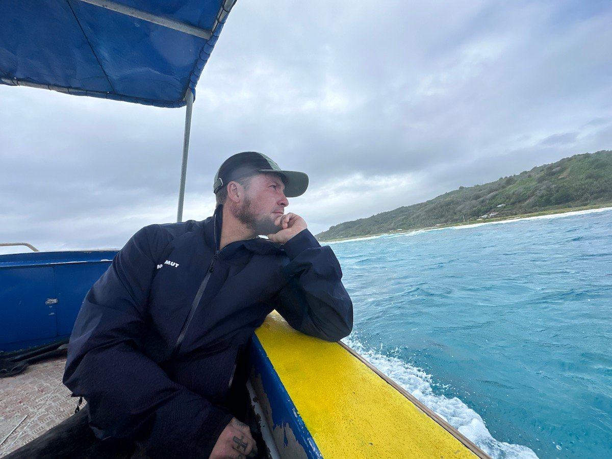 will leaning on the edge of a wooden boat looking out at the turquoise water in french polynesia