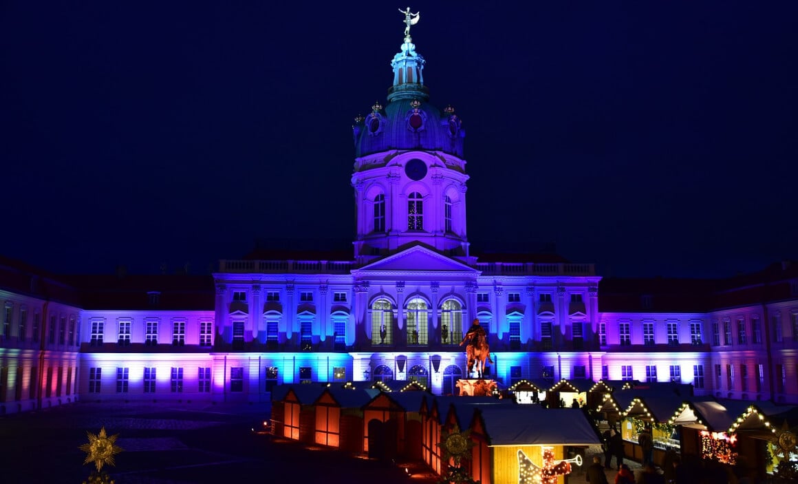 berlin christmas market with the building behind it lit up in purple and blue