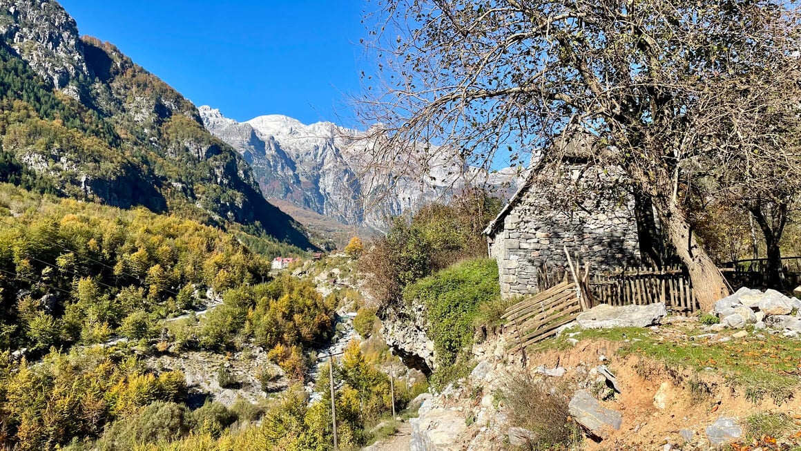 light yellow and green trees anda stone cottage on a blue sky day in the albanian alps