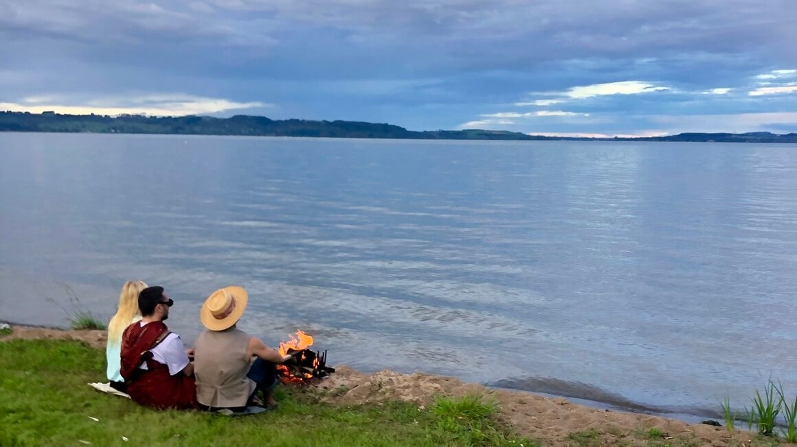 Friends sitting by a lake in Rotorua, New Zealand with a campfire