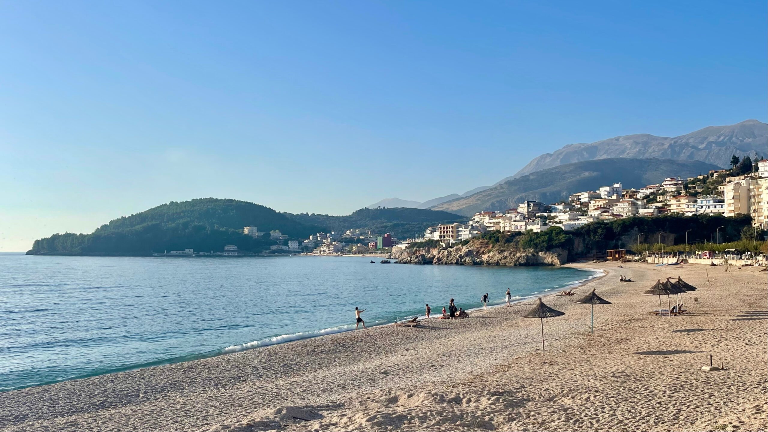 people walking along a beach in himare, albania