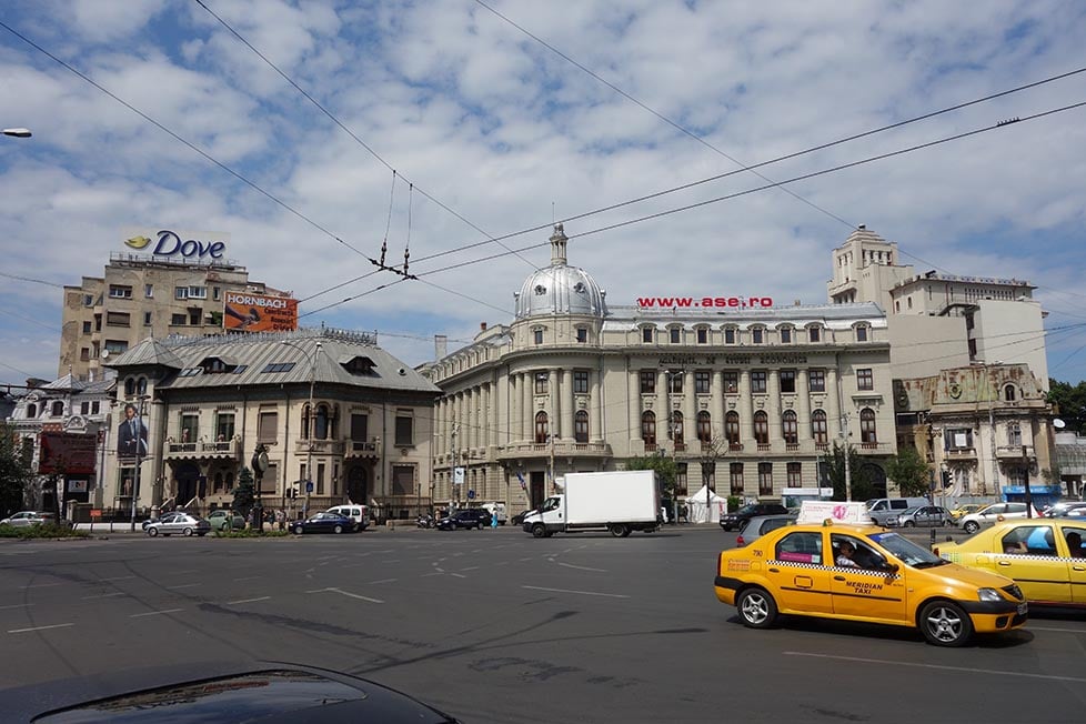 Taxis drive under trolleybus lines on a wide road in Bucharest, Romania with some old ornate buildings behind