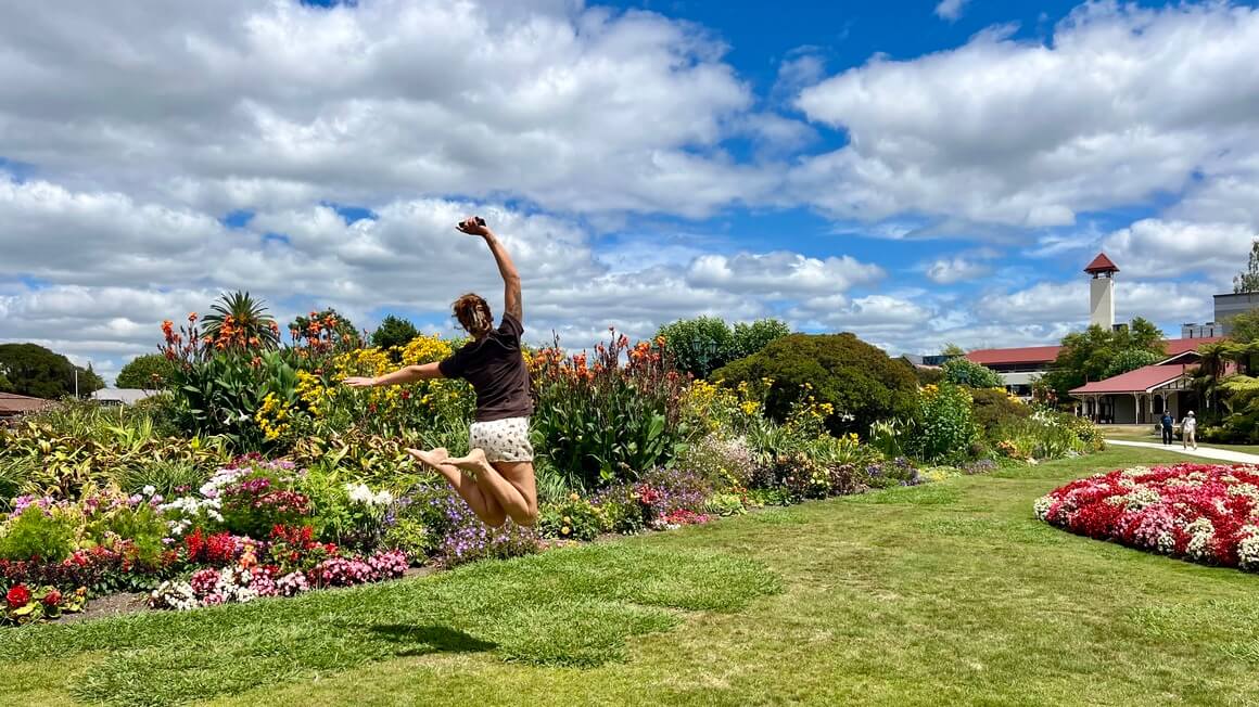 Girl jumping in front of a flower garden in Rotorua government gardens, New Zealand