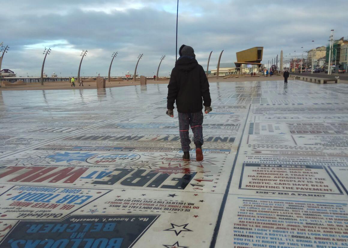 Man walking on the comedy strip on Blackpool front in winter clothes on an overcast day