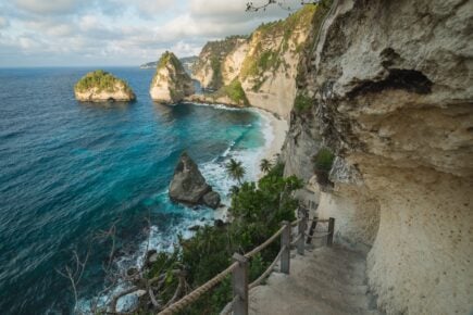 stone staircase leading down cliffs to a bright blue sea beach in nusa penida