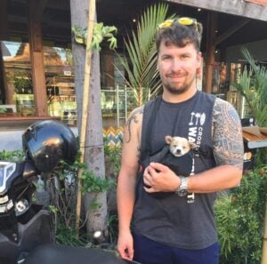 Will standing next to a scooter with a puppy in a small bag he is wearing in Bali, Indonesia