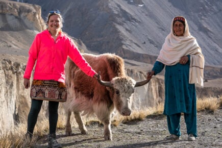 Samantha and a woman standing next to a yak in the mountain of Pakistan