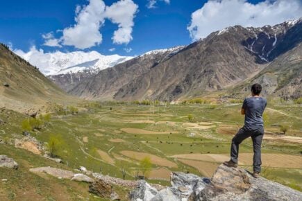 A person is standing on a rock above a valley with mountains either side in Pakistan