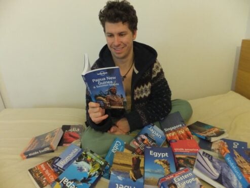 Will sitting next to a pile of lonely planet travel guide books on a bed