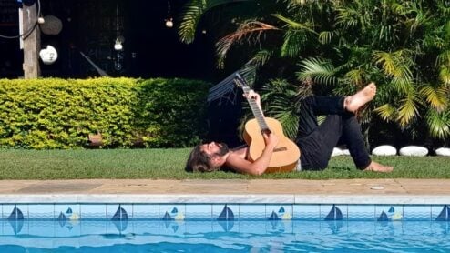 a man playing guitar by the pool at a hostel in buzios, brasil