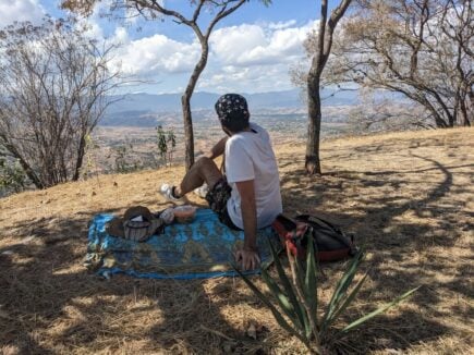 Man sat facing the vista over the city from a patch of shade on a dry hill