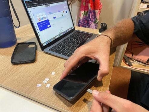 A person putting a sim card into a phone next to a laptop with a pile of plastic sim cards next to them and a phone case.