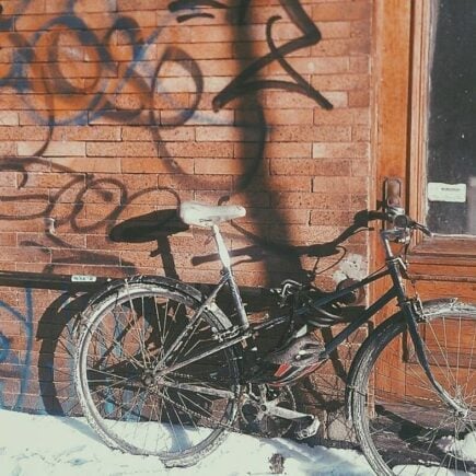 a bicycle sitting in snow next to a brick wall covered in graffiti in montreal canada