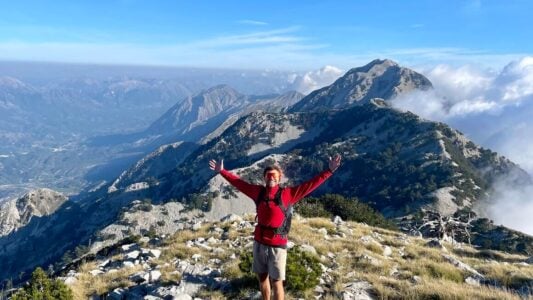 person at the top of a mountain in Albania smiling with arms open wide